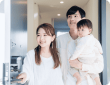 ドアを開ける母親と後ろで赤ちゃんを抱っこする父親の写真
